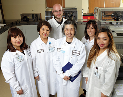 Dr. Ng (center) with her point-of-care testing team. From left: lab operations manager Feuy Saechao, POC testing coordinator Marian Castillo, LIS analyst Jesse Genosick, clinical laboratory scientist Doro Goto, and chemistry specialist Kristine Claire Fernandez.