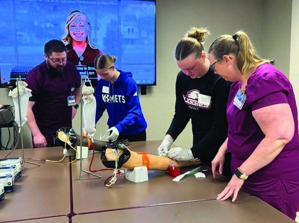 Students practice performing blood draws using a mannequin.